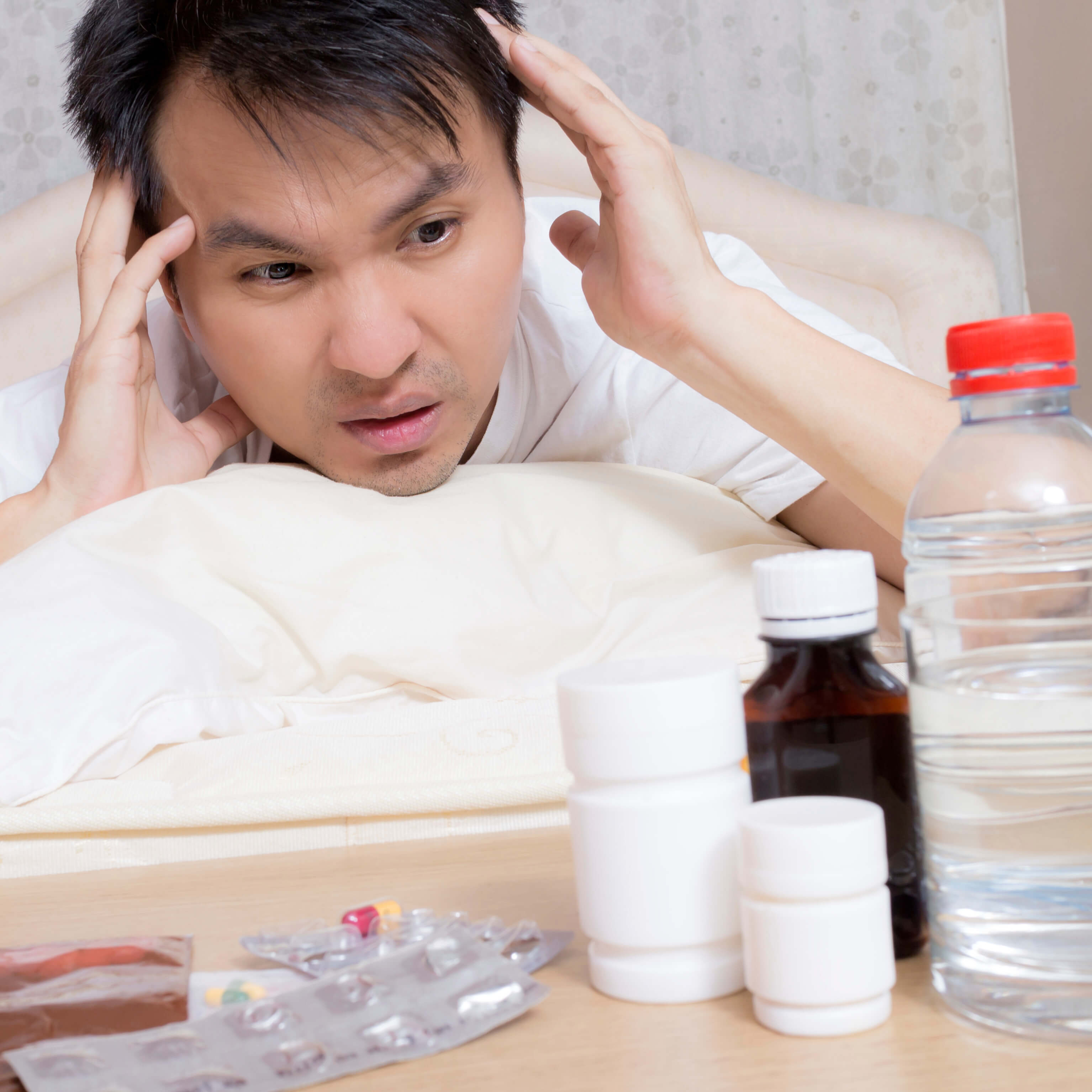 Asian Handsome Man in bed with tablets and water suffering insomnia, hangover and headache
