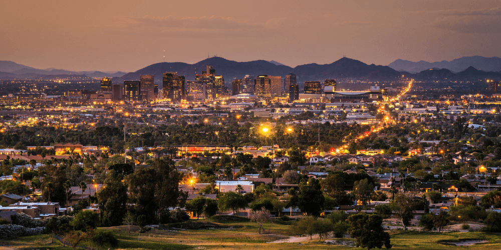 Silhouette of Phoenix skyline with tall buildings against a dark sunset sky.