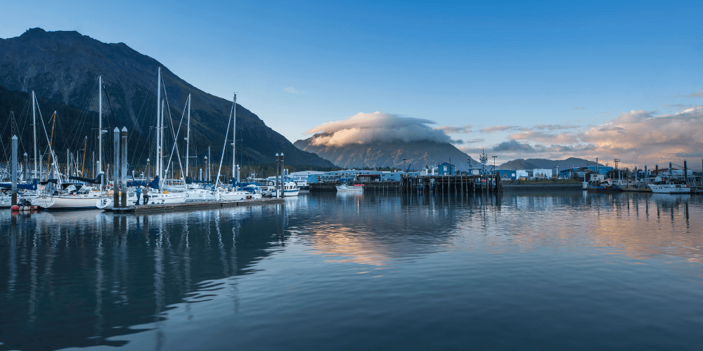 Seward, Alaska, filled with fishing boats and sailboats, surrounded by scenic coastal mountains.