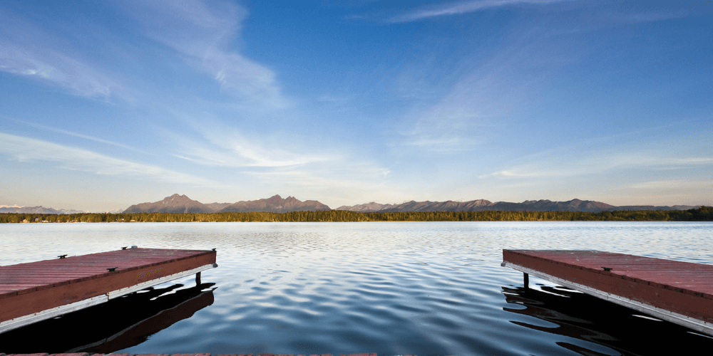 Vibrant sunset over Wasilla, Alaska, reflecting on a tranquil lake in the foreground.